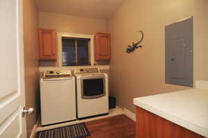 Laundry area with dark hardwood / wood-style flooring, electric panel, cabinets, and washing machine and dryer