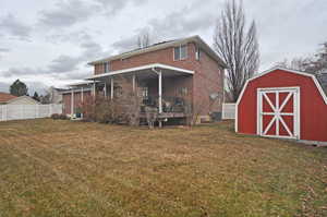 Rear view of house with a storage shed, a lawn, and a porch