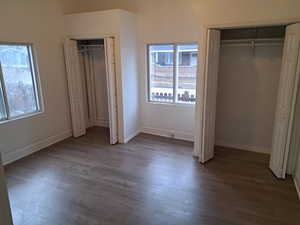 Unfurnished bedroom with hardwood / wood-style floors, multiple windows, and two closets