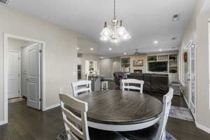 Dining room with a large fireplace, ceiling fan with notable chandelier, dark hardwood / wood-style floors, and built in shelves