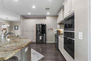 Kitchen featuring sink, hanging light fixtures, light stone counters, black appliances, and white cabinets