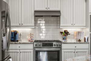 Kitchen with extractor fan, appliances with stainless steel finishes, tasteful backsplash, white cabinets, and light stone counters