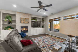 Living room featuring built in shelves, a fireplace, and ceiling fan