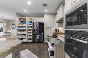 Kitchen featuring pendant lighting, white cabinetry, stainless steel refrigerator with ice dispenser, light stone counters, and built in microwave