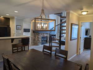 Dining space featuring ornamental molding, a stone fireplace, carpet floors, and a chandelier