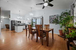 Dining room with lofted ceiling, ceiling fan with notable chandelier, light hardwood / wood-style flooring, and a textured ceiling