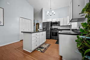 Kitchen with sink, white cabinetry, hanging light fixtures, appliances with stainless steel finishes, and a kitchen island