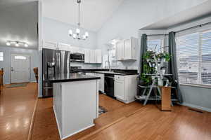 Kitchen with appliances with stainless steel finishes, pendant lighting, white cabinets, a center island, and light hardwood / wood-style floors