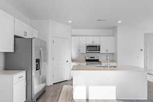 Kitchen featuring an island with sink, stainless steel appliances, sink, and white cabinets