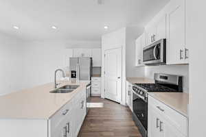 Kitchen featuring stainless steel appliances, white cabinetry, sink, and a kitchen island with sink