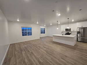 Kitchen with white cabinetry, stainless steel appliances, hanging light fixtures, and a center island with sink