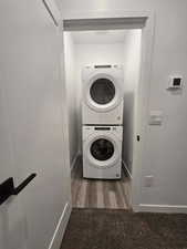 Laundry room with stacked washer and clothes dryer and dark hardwood / wood-style floors