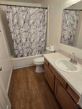 Full bathroom with vanity, hardwood / wood-style floors, shower / bath combination with curtain, and toilet