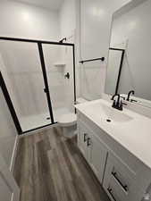 Bathroom featuring wood-type flooring, toilet, a shower with shower door, and vanity