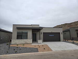 View of front of property featuring a garage, concrete driveway, stone siding, and stucco siding