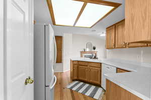 Kitchen featuring sink, white appliances, light hardwood / wood-style floors, vaulted ceiling, and kitchen peninsula