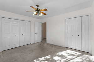 Unfurnished bedroom featuring two closets, light carpet, and ceiling fan