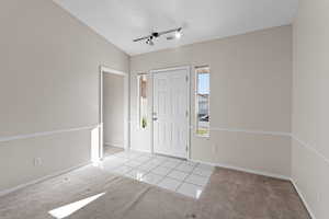 Foyer featuring track lighting, vaulted ceiling, light carpet, and a textured ceiling