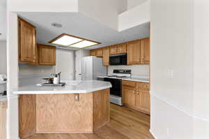 Kitchen with light hardwood / wood-style flooring, range with electric cooktop, white refrigerator, a textured ceiling, and kitchen peninsula