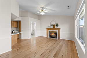 Unfurnished living room with a tiled fireplace, light hardwood / wood-style flooring, and ceiling fan