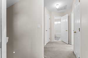 Hall with light colored carpet and a textured ceiling