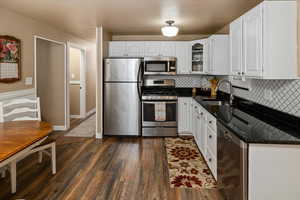 Kitchen featuring dark hardwood / wood-style floors, tasteful backsplash, sink, white cabinets, and stainless steel appliances