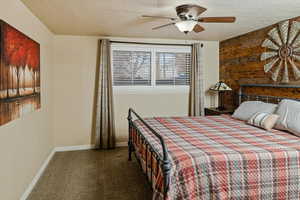 Carpeted bedroom featuring ceiling fan, a textured ceiling, and wood walls