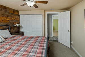 Unfurnished bedroom with wooden walls, carpet floors, ceiling fan, a textured ceiling, and a closet