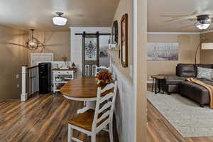 Dining space with dark hardwood / wood-style floors, ornamental molding, a barn door, and ceiling fan