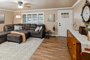 Living room featuring dark wood-type flooring, ornamental molding, and ceiling fan