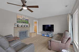 Living room with ceiling fan, a stone fireplace, and hardwood flooring