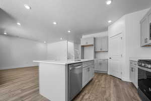 Kitchen with sink, appliances with stainless steel finishes, a kitchen island with sink, a textured ceiling, and light wood-type flooring