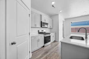 Kitchen featuring appliances with stainless steel finishes, sink, a textured ceiling, and light wood-type flooring