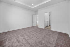 Unfurnished bedroom featuring a tray ceiling, light colored carpet, and ensuite bathroom