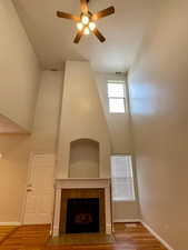 Unfurnished living room featuring a tiled fireplace, hardwood / wood-style floors, ceiling fan, and a high ceiling