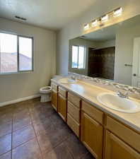 Bathroom with tiled shower, vanity, toilet, and tile patterned flooring