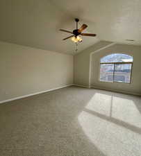 Carpeted spare room featuring ceiling fan and vaulted ceiling
