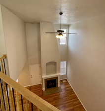 Unfurnished living room featuring hardwood / wood-style flooring, ceiling fan, a fireplace, and a textured ceiling