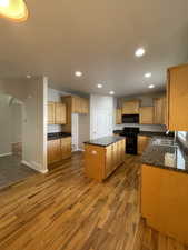 Kitchen featuring sink, dark stone countertops, hardwood / wood-style floors, black appliances, and a kitchen island