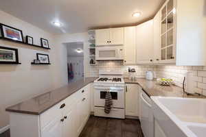 Kitchen with Quartz counters, white appliances, kitchen peninsula, and white custom cabinets.