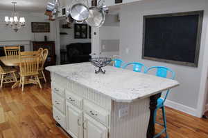 Kitchen with a breakfast bar area, decorative light fixtures, a center island, light hardwood / wood-style flooring, and white cabinets