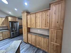 Kitchen with dark hardwood / new wood-style flooring, stainless steel fridge with ice dispenser, and vaulted ceiling