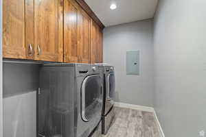 Laundry room with light hardwood / wood-style flooring, washer and clothes dryer, electric panel, and cabinets