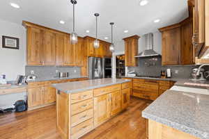 Kitchen with a kitchen island, appliances with stainless steel finishes, pendant lighting, sink, and wall chimney range hood