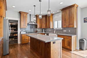 Kitchen featuring wall chimney exhaust hood, sink, a center island, hanging light fixtures, and appliances with stainless steel finishes