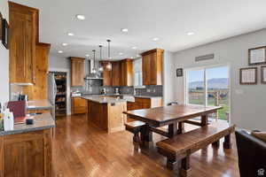 Kitchen featuring wall chimney range hood, hanging light fixtures, a center island, light stone counters, and a mountain view