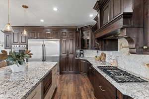 Kitchen with stainless steel appliances, dark hardwood / wood-style flooring, hanging light fixtures, and light stone counters