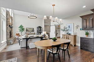 Dining space featuring a barn door, dark wood-type flooring, a stone fireplace, and an inviting chandelier