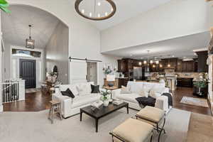 Living room featuring dark hardwood / wood-style floors, a barn door, a chandelier, and high vaulted ceiling