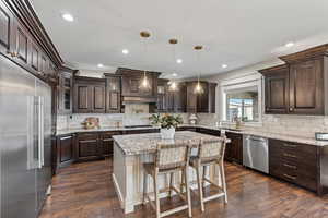 Kitchen with appliances with stainless steel finishes, sink, hanging light fixtures, a center island, and dark wood-type flooring